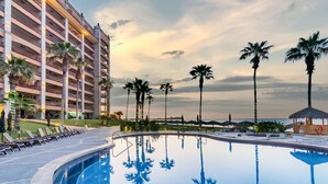 A hotel with a large pool, palm trees, and a sunset view.