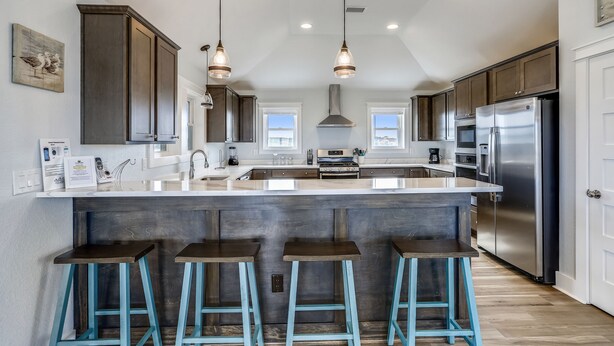 A modern kitchen with dark wooden cabinets, a large island with bar stools, stainless steel appliances, and pendant lighting. - Semi Oceanfront New pool, Ocean Views. (Kill Devil Hills)