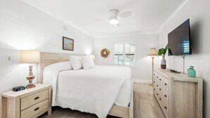 A bedroom with a bed, bedside tables, a dresser, a TV, and a window with blinds.