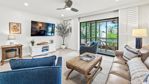 A modern living room with a flat-screen TV, comfortable seating, a ceiling fan, and a view of the outdoors.