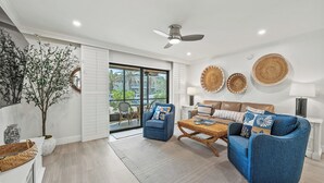 A spacious living room with a blue sofa set, a coffee table, and a ceiling fan.