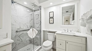 A modern bathroom with a glass shower enclosure, a toilet, a sink, and a vanity with drawers.
