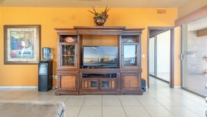 A living room with a wooden entertainment center, a flat-screen TV, and a water dispenser.
