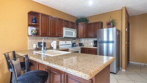 A kitchen with granite countertops, wooden cabinets, a stainless steel refrigerator, a microwave, a stove, and a sink.