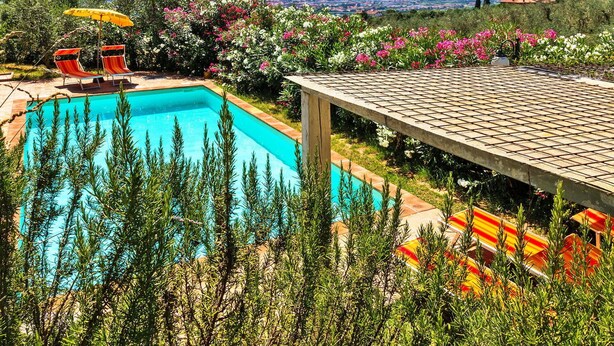 A swimming pool with two lounge chairs and an umbrella, surrounded by lush greenery and flowers. - Beautiful private villa with A/C, WIFI, hot tub, private pool, TV, patio and pets allowed (Montecatini Terme)