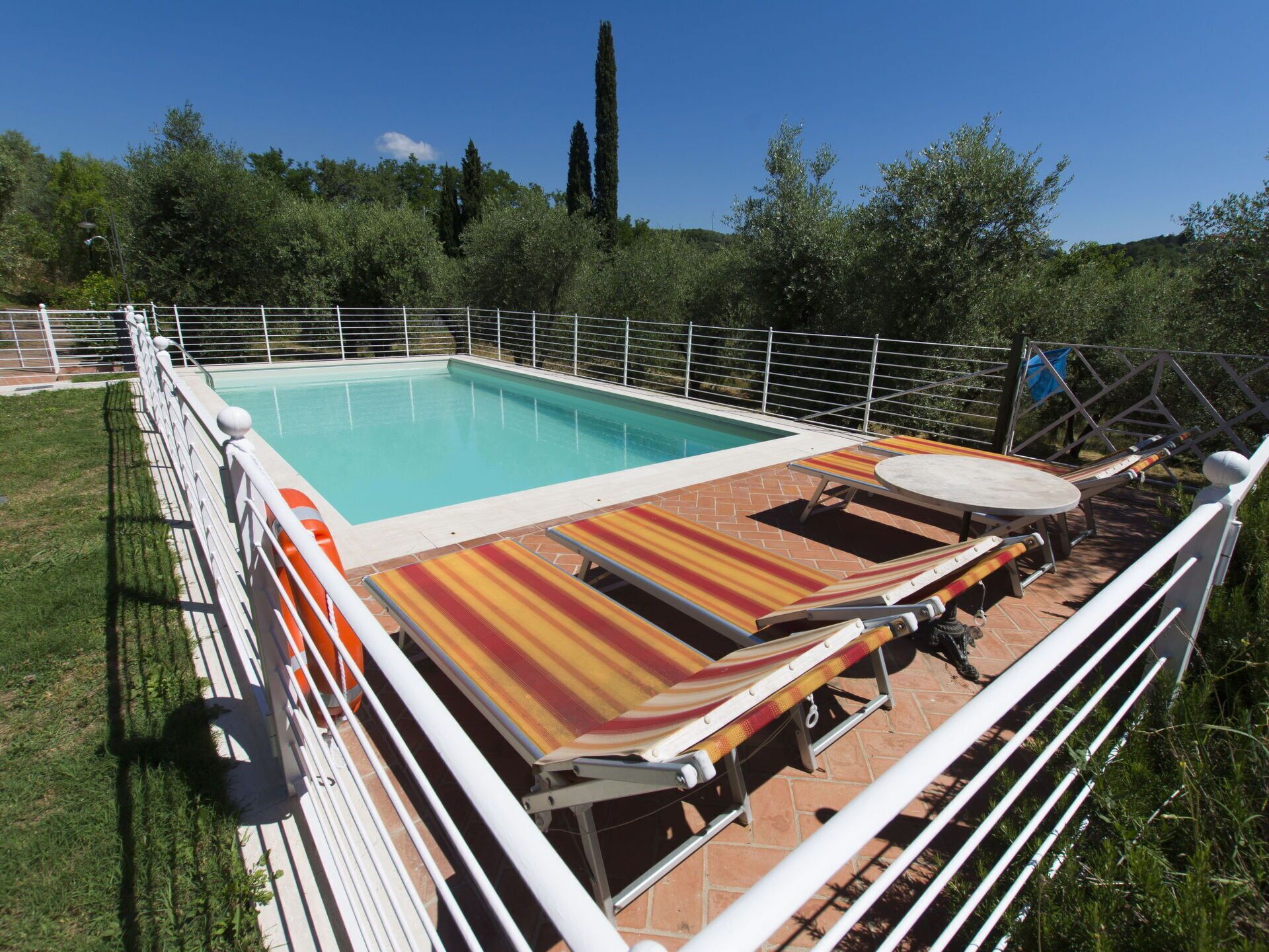 Une piscine rectangulaire dotée d’une terrasse carrelée, entourée d’une clôture en métal blanc.