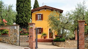 Eine gelbe Villa mit Steintor, Ziegelbogen und einer kleinen Veranda mit Blumentöpfen.