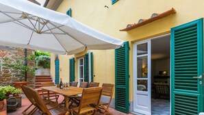 A patio with a wooden table and chairs, green shutters, and a white umbrella.