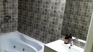Casa de banho com banheira independente, lavatório com espelho e azulejos estampados nas paredes.