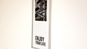 Um letreiro emoldurado com o texto 'CURTA A VIDA' e uma fotografia em preto e branco de uma rua.