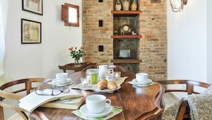 Un comedor con chimenea de ladrillo, una mesa de madera dispuesta para el desayuno y cuadros en la pared.