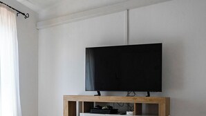 Ein modernes Wohnzimmer mit Flachbildfernseher auf einem Holz-TV-Möbel, weißen Schränken und einem Fliesenboden.