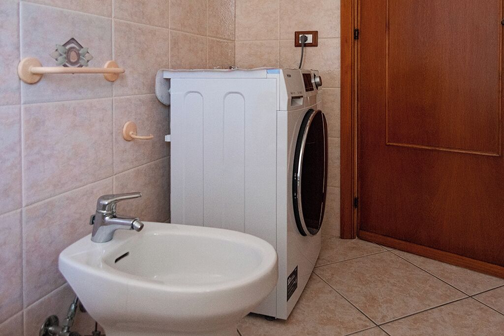 A compact bathroom with a white sink, a washing machine, and a wooden door.