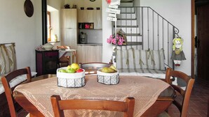 A dining area with a round table, chairs, and a fruit basket. There is a kitchen in the background with cabinets and a stove. A staircase is visible to the right. - Wonderful private villa for 2 people with WIFI, TV and terrace (Volterra)