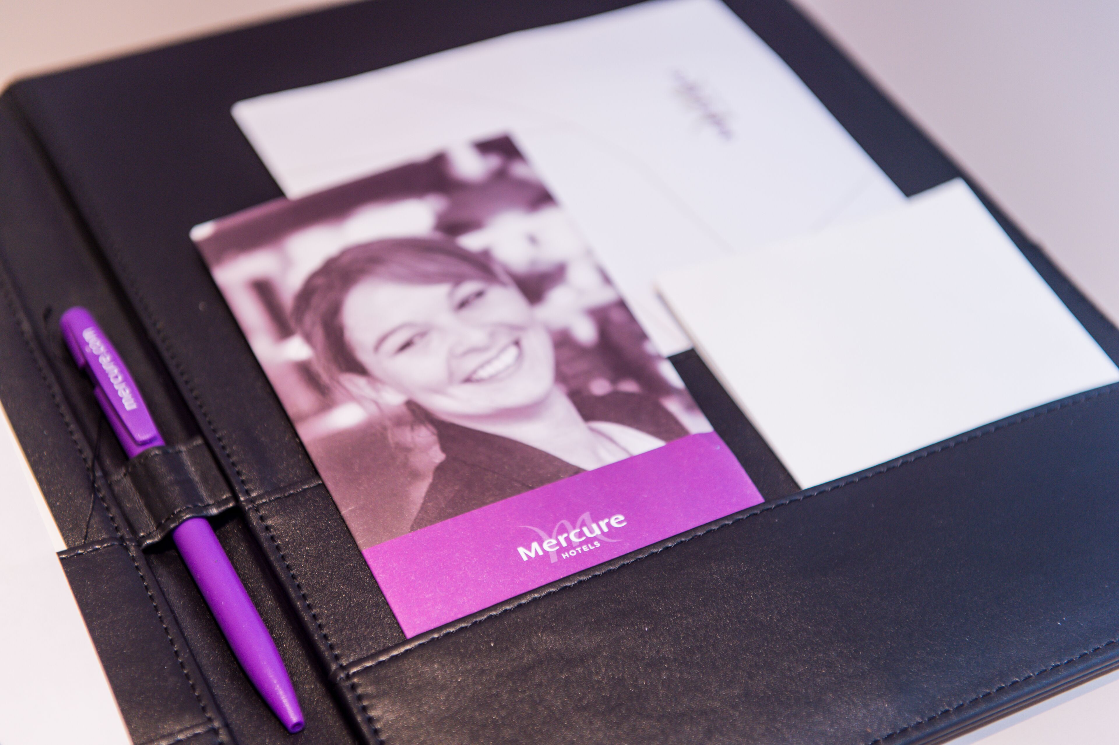 A black leather-bound notebook with a purple pen and a business card for Mercure Hotels.