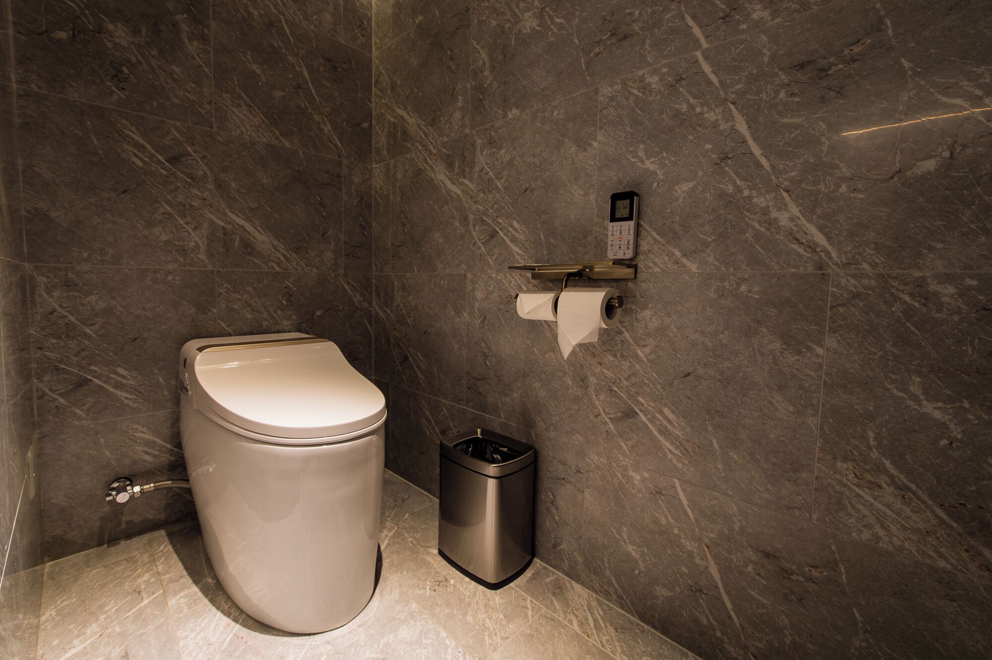 A bathroom with a toilet, a trash bin, and a toilet paper holder on the wall.