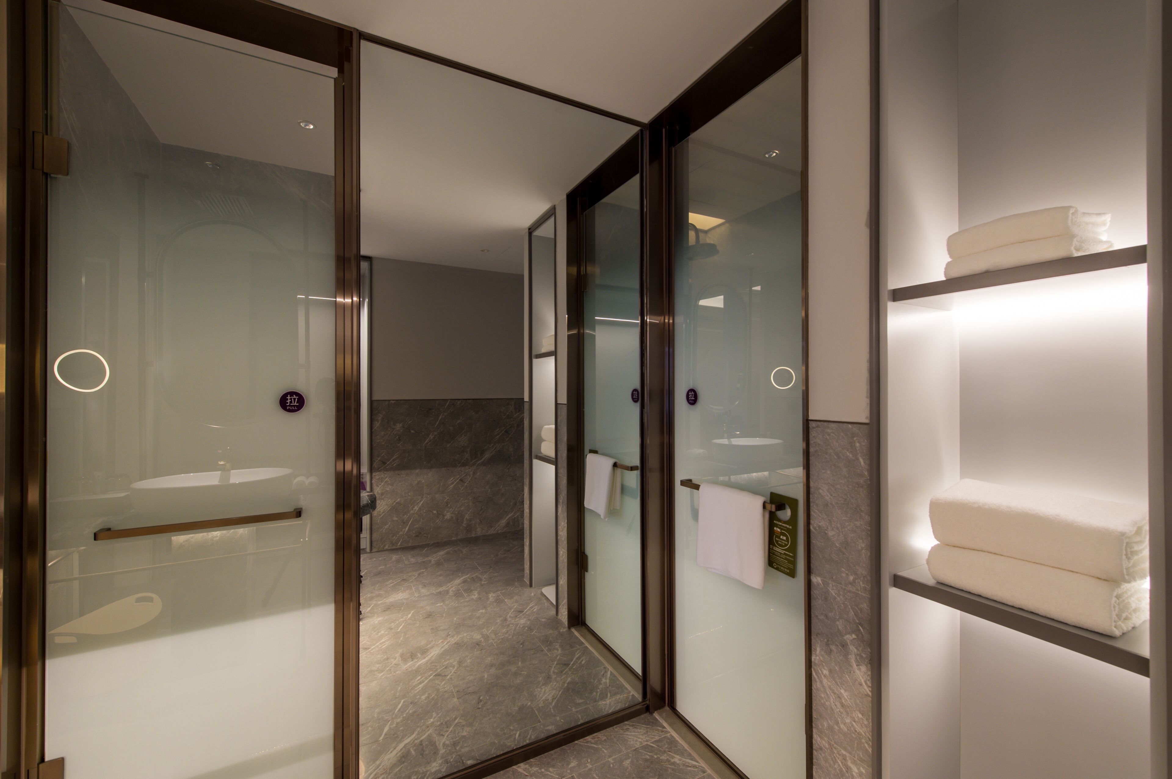 Un baño moderno con ducha envuelta en vidrio, suelo de mármol y repisa con toallas dobladas.