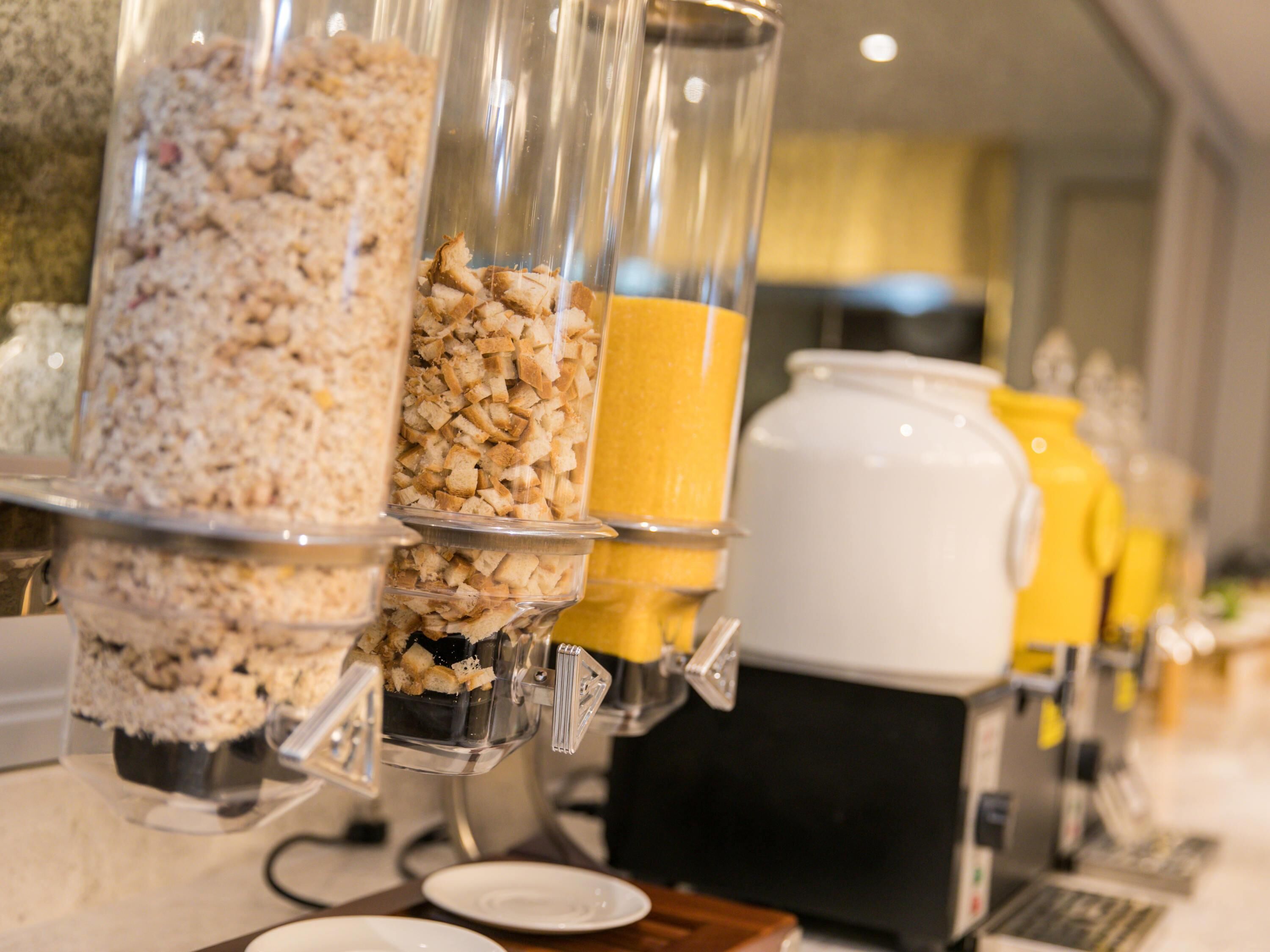 Disposición de un bufé con varios recipientes de comida, incluyendo cereales y jugo de naranja.