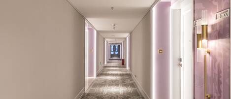 A hallway with patterned carpet, a door with a number sign, and a light fixture on the wall.