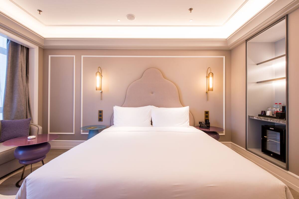 A hotel room with a large bed, bedside tables, a desk, and a minibar.