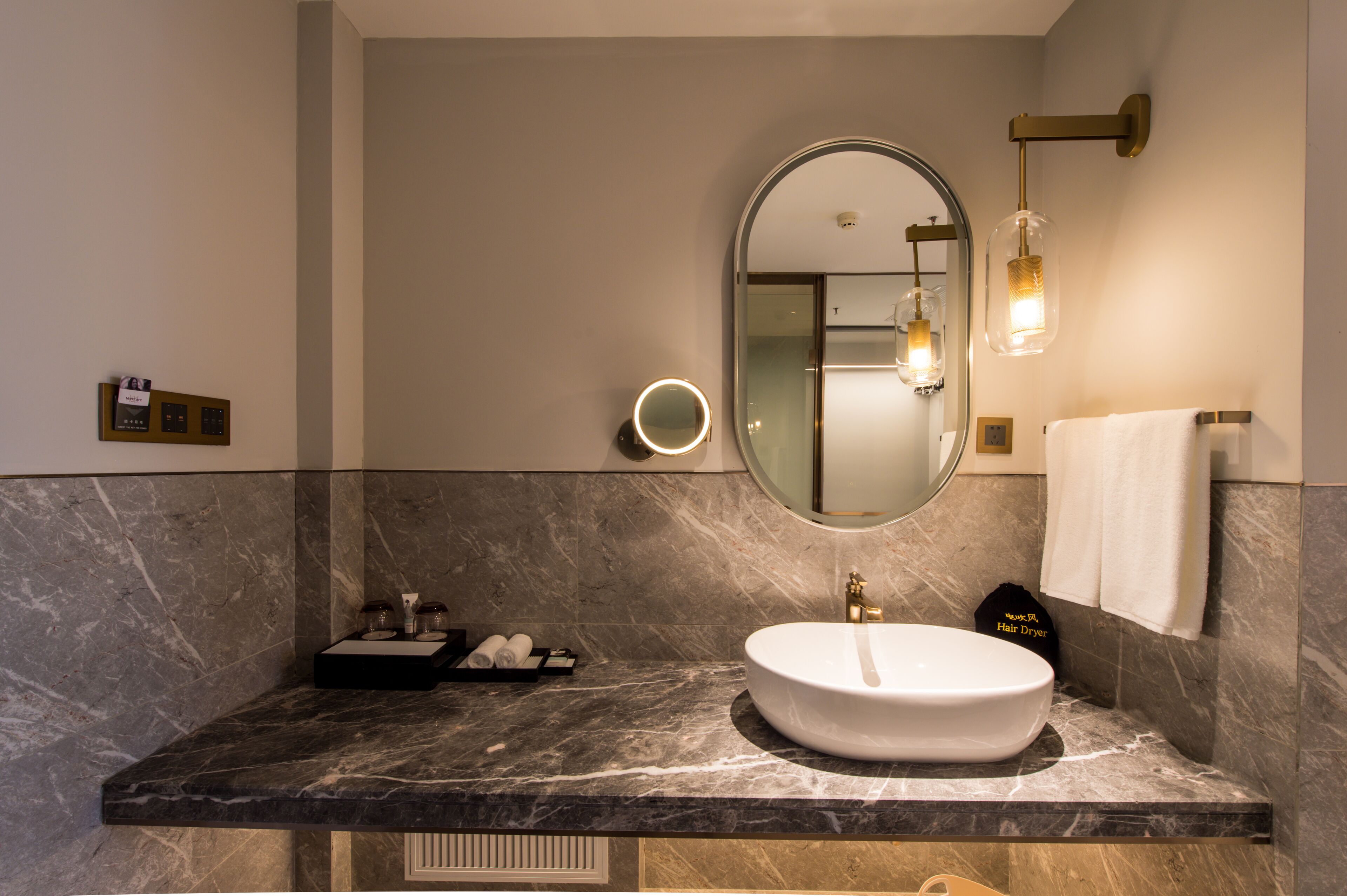 Un baño moderno con encimera de mármol, un espejo redondo con luz y un lavabo blanco.