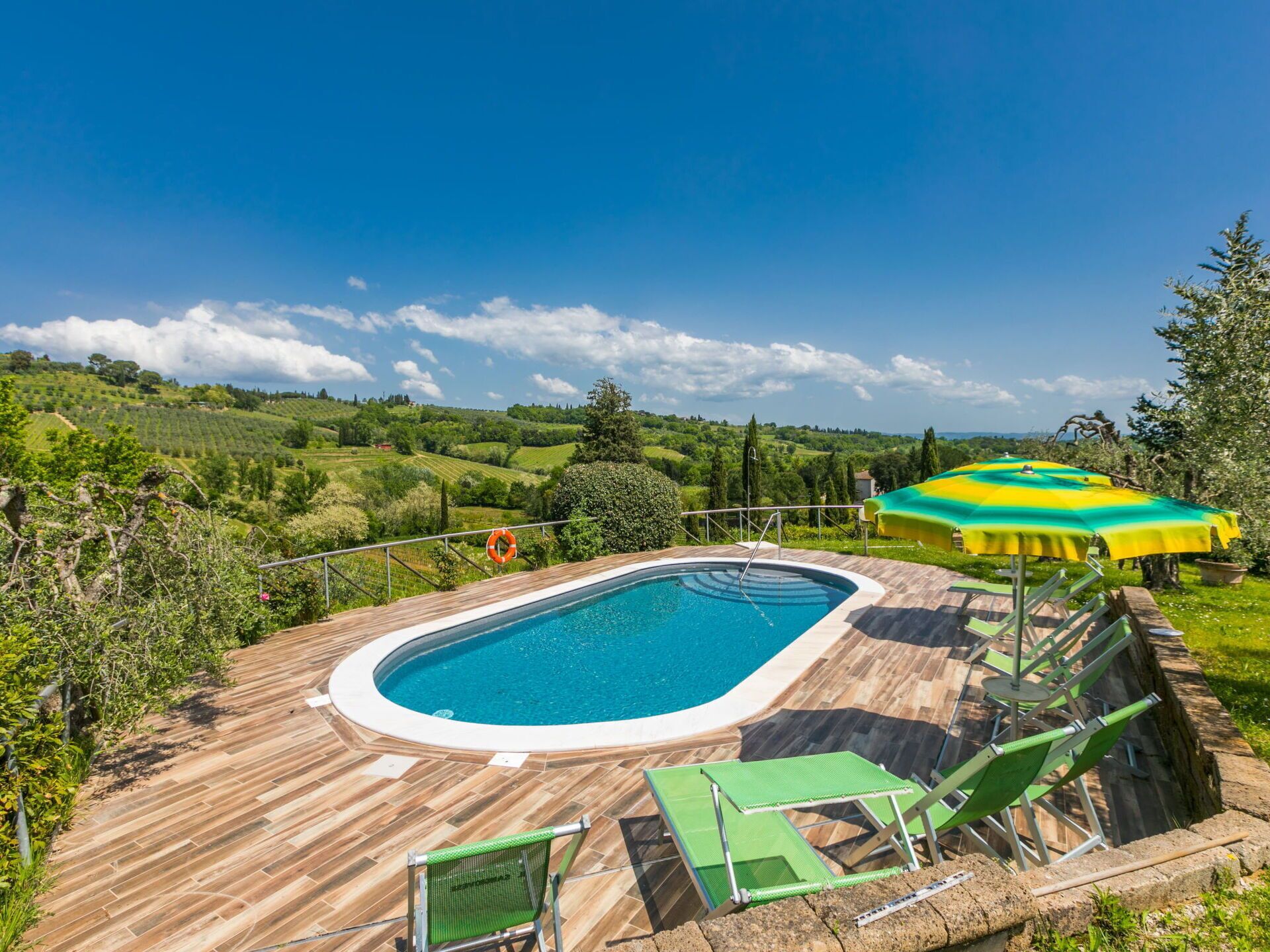 Une piscine dotée d’une terrasse en bois, entourée d’une végétation luxuriante et avec des collines en arrière-plan.