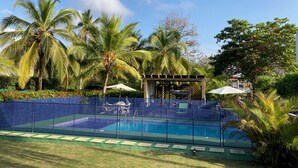 Una piscina rodeada de palmeras y una pérgola con sombrillas.