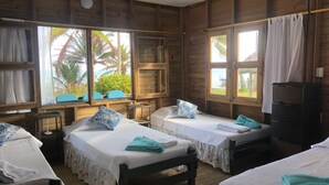 Una cabaña de madera con dos camas, cada una con una almohada y una toalla doblada. Tiene ventanas con cortinas, una mesita y un estante.