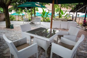 An outdoor patio with white wicker furniture, a glass table, and green umbrellas. - La Villa Cafe & Suites (Kigali)
