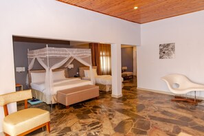A bedroom with a canopy bed, a bench, a chair, and a stone-tiled floor. - La Villa Cafe & Suites (Kigali)