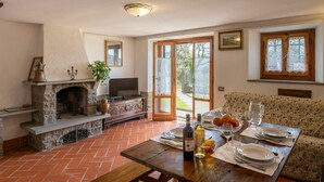 Zona pranzo con camino in pietra, televisore e tavolo apparecchiato per due, completo di bicchieri da vino e piatti.