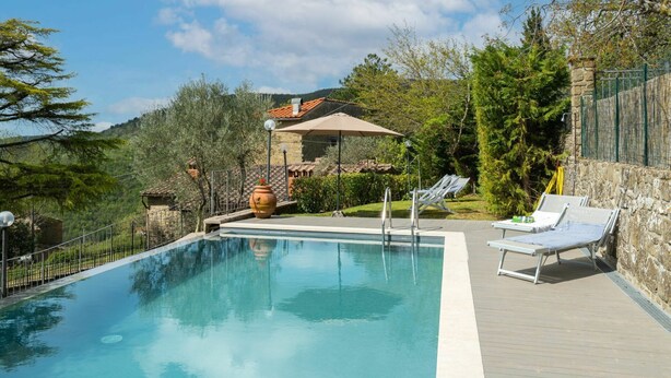 Una piscina con lettini e a bordo una parete in pietra.