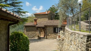 Un edificio in pietra con tetto in tegole, un piccolo portico e un cortile pavimentato.