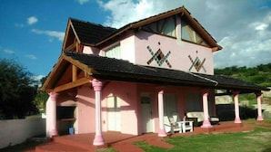 A pink house with a covered porch and a tiled roof. - Cabañas & Apart Yki Shamuaika (Capilla del Monte)