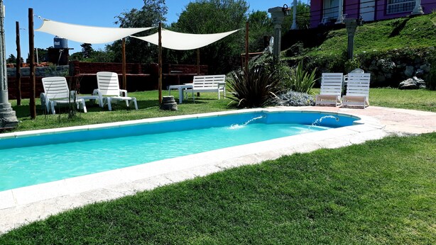 A swimming pool with white lounge chairs and a canopy. - Cabañas & Apart Yki Shamuaika (Capilla del Monte)