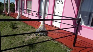 A pink building with white doors and columns, a red pathway, and a metal fence. - Cabañas & Apart Yki Shamuaika (Capilla del Monte)