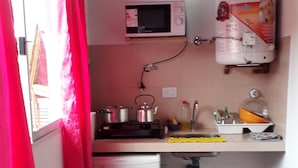A compact kitchen with a microwave, sink, and water heater. There's a table with a floral tablecloth and a chair. - Cabañas & Apart Yki Shamuaika (Capilla del Monte)
