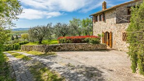 Une maison en pierre avec une allée pavée, entourée de verdure et d’arbres.