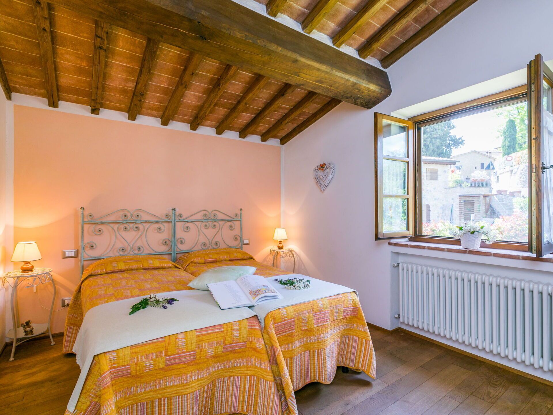 Een slaapkamer met twee bedden, een houten plafond, een raam met uitzicht en een radiator.