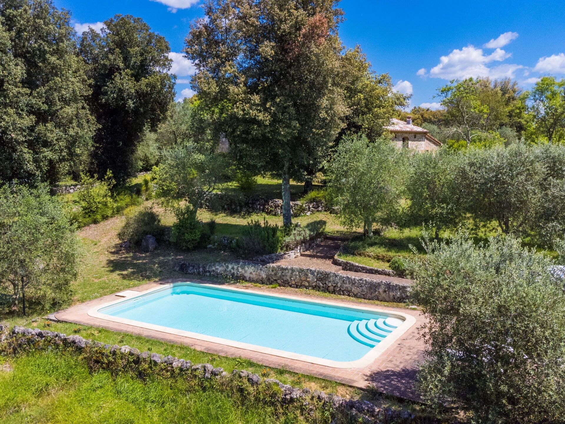 Une piscine rectangulaire entourée d’un mur de pierre, avec un bâtiment en pierre en arrière-plan.