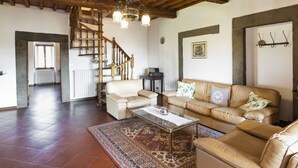 Een ruime woonkamer met een hoog houten plafond, een trap, een beigekleurige zithoek en een kamerbreed tapijt.
