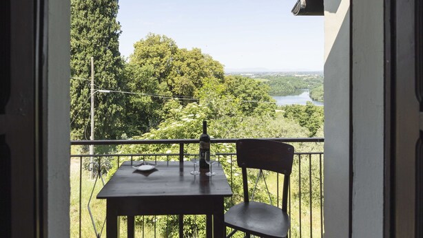Een balkon met een tafel en stoel, met uitzicht op een rivier en een bebost landschap.