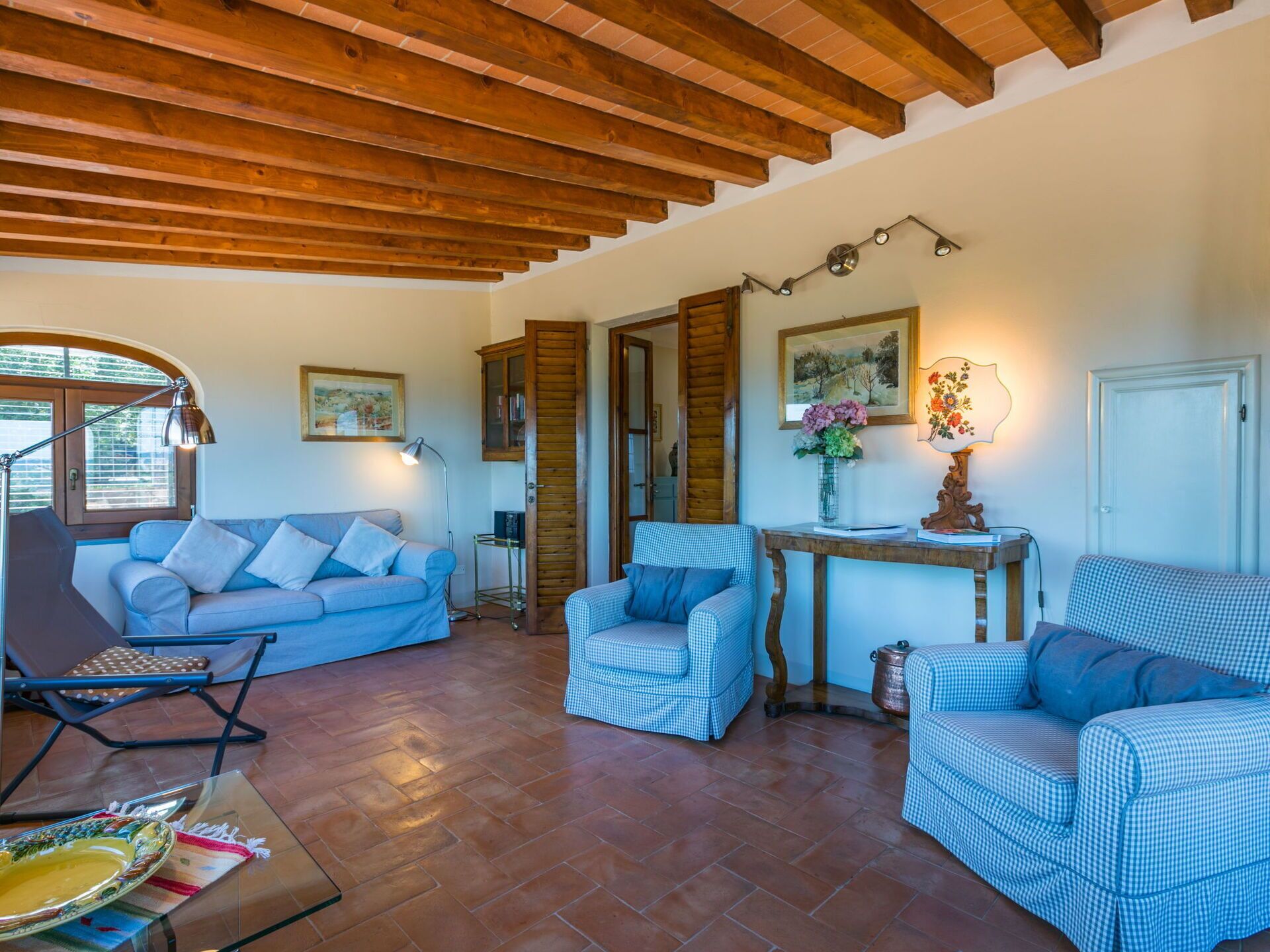 Un salon chaleureux avec un plafond en bois, un canapé bleu, un fauteuil à carreaux et une petite table sur laquelle est posé un vase de fleurs.
