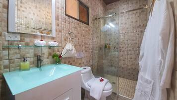 Casa de banho com cabine de chuveiro em vidro, pia branca com bancada azul e sanita com toalha branca e uma rosa.