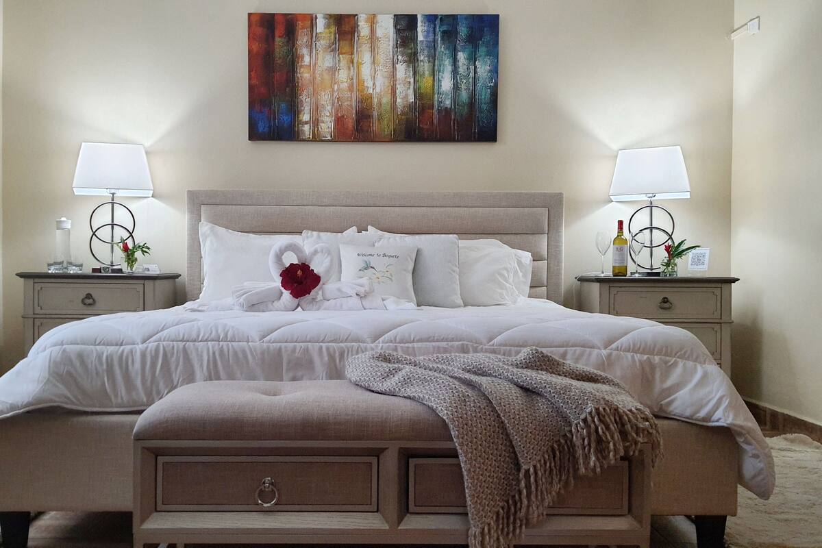 A neatly made bed with a swan-shaped pillow, a decorative swan, and a welcome pillow. There are two bedside tables with lamps and a vase of flowers.