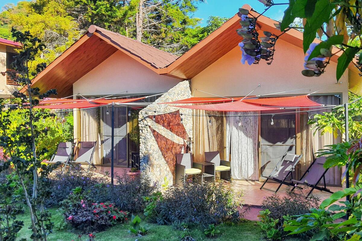 A house with a stone wall, a wooden roof, and a patio with two chairs and a table.