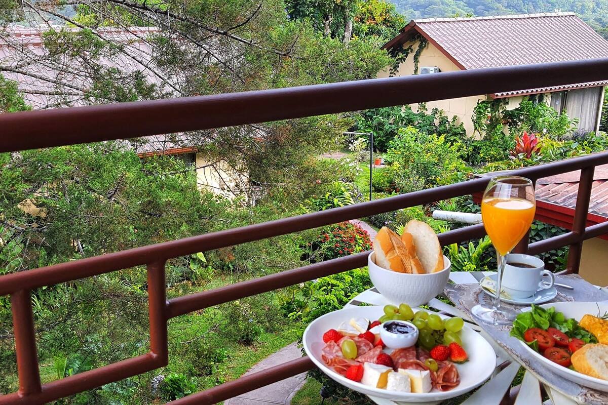 A balcony with a table set for breakfast, including a plate of cheese, grapes, and bread, a glass of orange juice, and a cup of coffee.