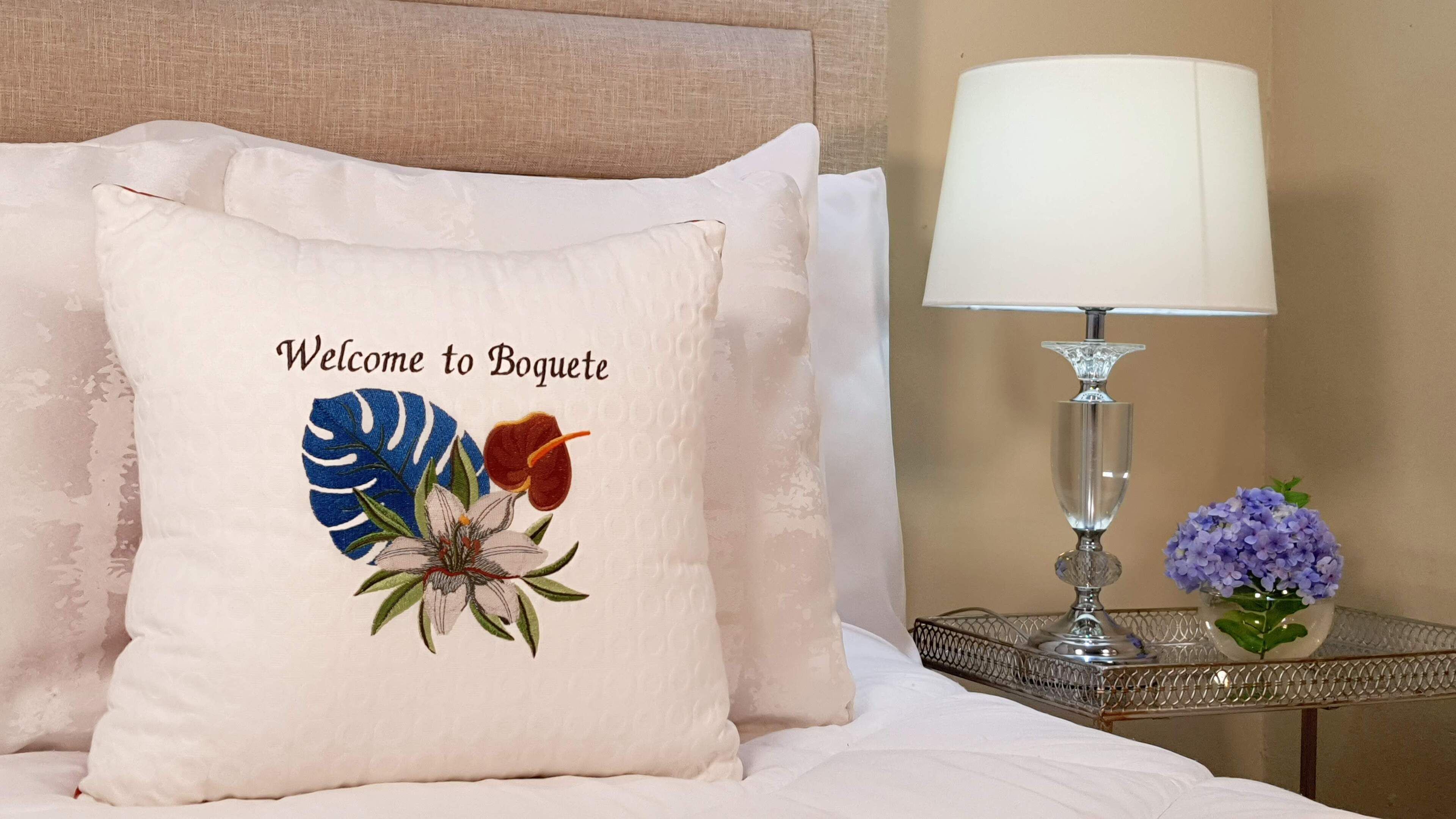 A bed with a pillow featuring a floral design and the text "Welcome to Boquete."