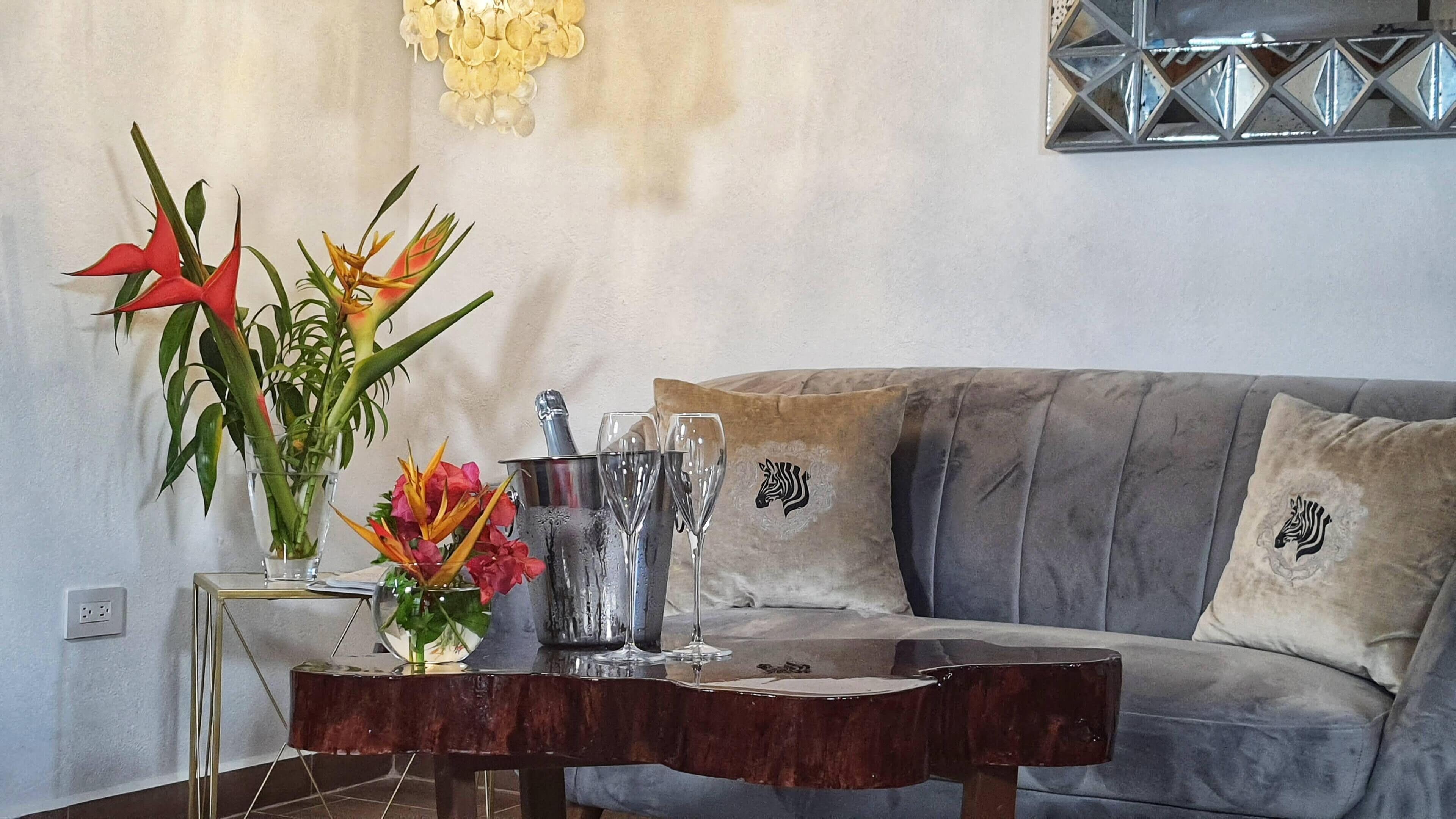 A living room with a grey sofa, two cushions with zebra prints, a small table with a vase of flowers, and a decorative wall piece.