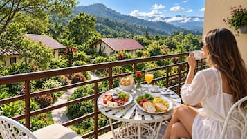 A balcony with a table set for breakfast, overlooking a mountainous landscape.
